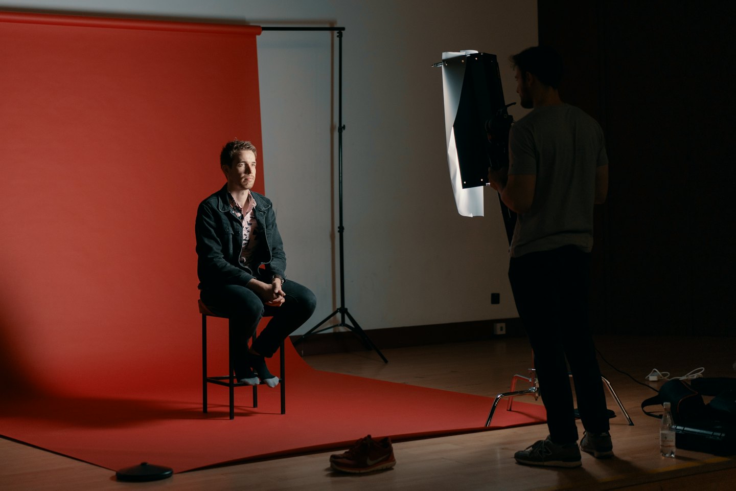 Mann sitzt auf einem Hocker vor rotem Hintergrund mit einem Fotografen.